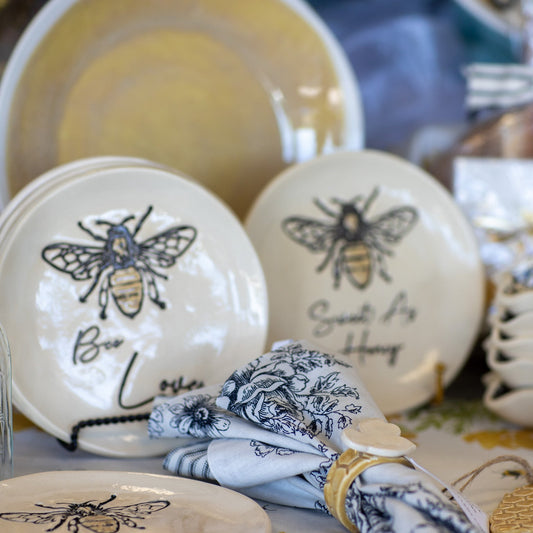 Decorative plates with bee designs and text on a table with other decorative items.